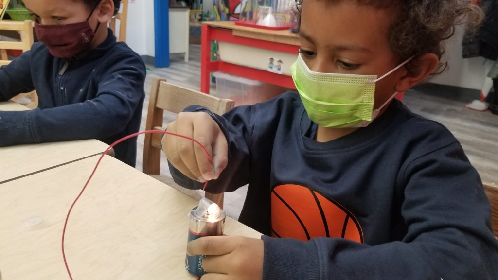 Student experimenting with a battery, light bulb, and wire.