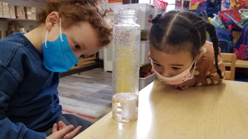 Two students observing condensation form in a glass tube.